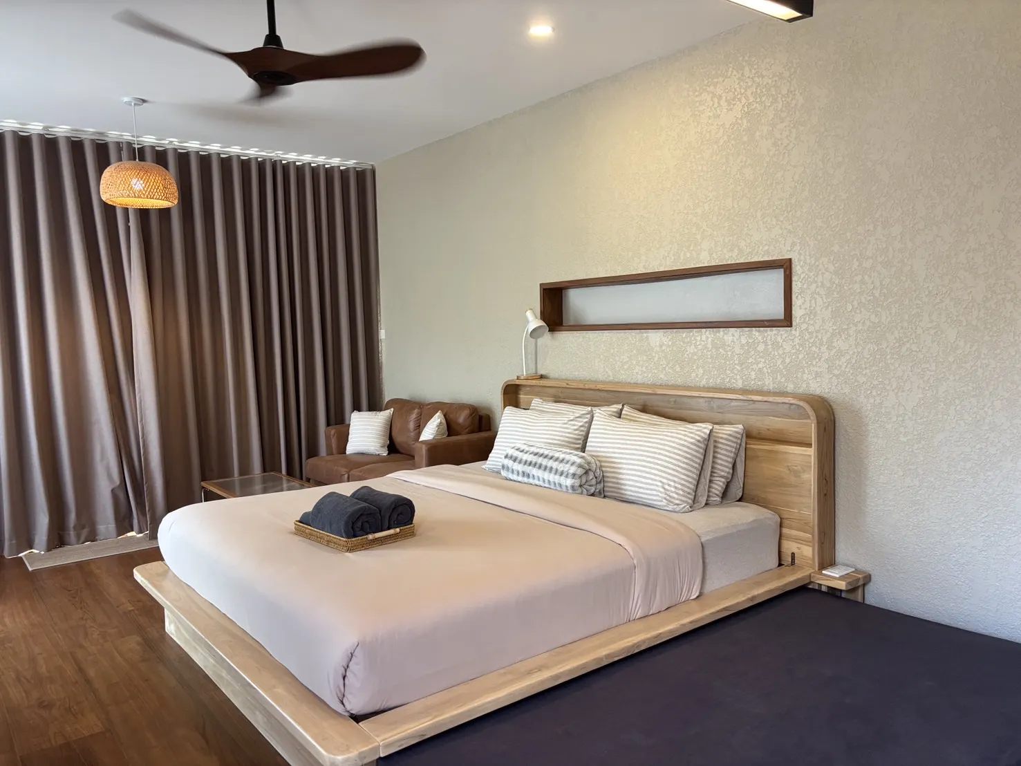 Bedroom with a low wooden bed, white linen and a ceiling fan